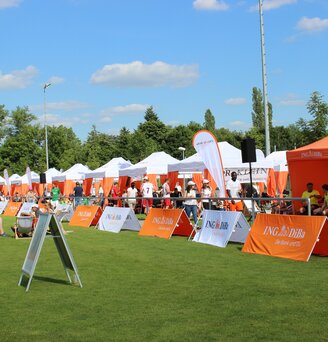 Serie van witte 6x3 m evenementen gazebos met oranje hoekgordijnen gepersonaliseerd met IngDiba logo en witte druppelvlaggen voor een buitenevenement