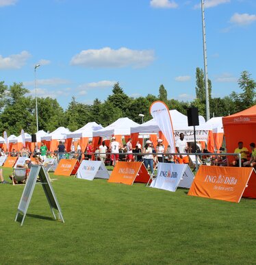 Serie van witte 6x3 m evenementen gazebos met oranje hoekgordijnen gepersonaliseerd met IngDiba logo en witte druppelvlaggen voor een buitenevenement