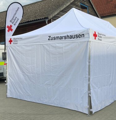 Witte 8x4 m gazebo met gesloten zijwanden en ramen, gepersonaliseerd met tekst voor Beierse Rode Kruis en gepersonaliseerde druppelvlag