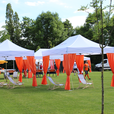 Weißer Ecotent® Faltpavillon 6x4 m mit orangefarbenen Vorhängen bei einer Outdoor-Veranstaltung.