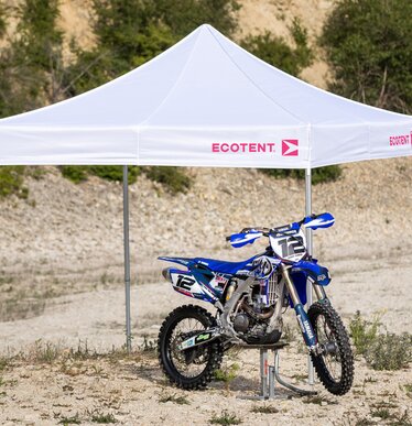 Witte 3x3 m Ecotent gazebo met fuchsia logo bedekt een blauwe motorcrossmotor in de woestijn